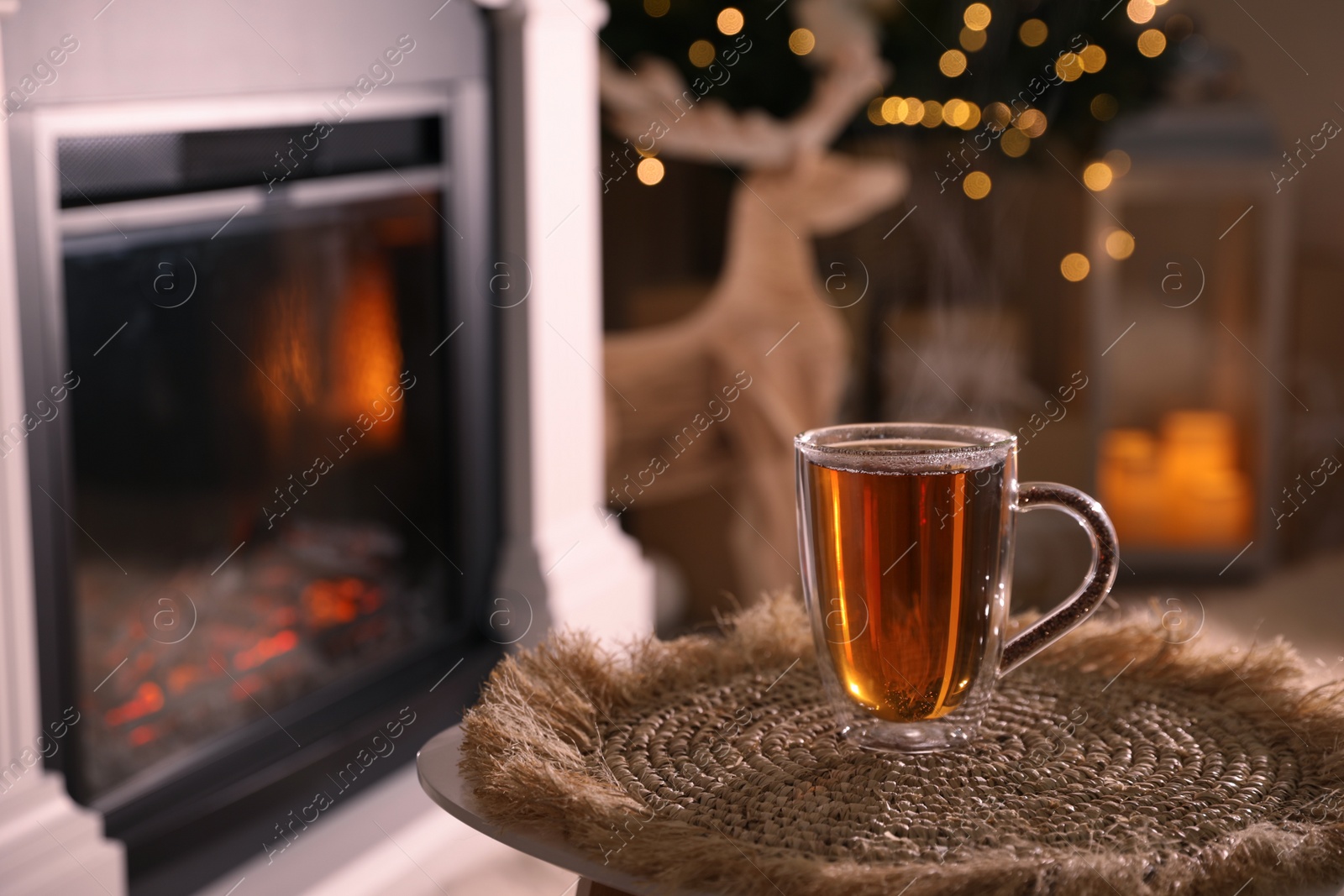 Photo of Glass of hot drink near fireplace in room. Space for text