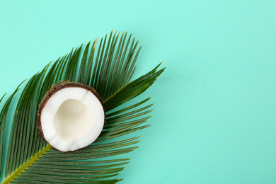 Half of ripe coconut and palm branch on turquoise background, top view. Space for text