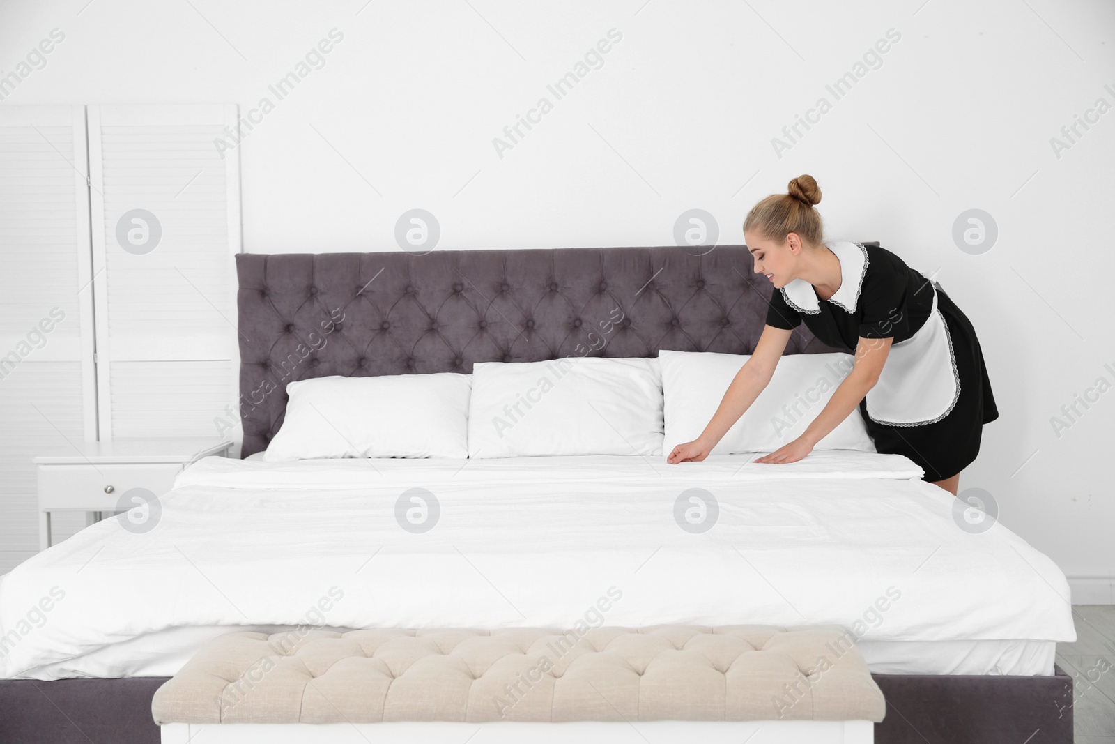 Photo of Young chambermaid making bed in hotel room