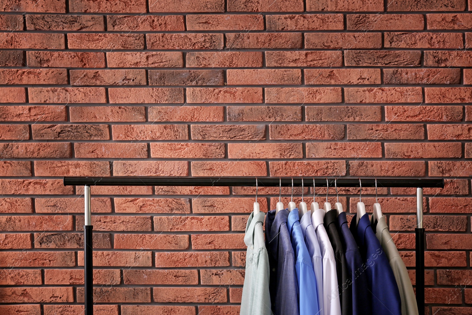 Photo of Wardrobe rack with stylish clothes near brick wall. Space for text