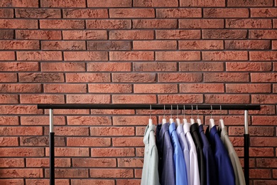 Wardrobe rack with stylish clothes near brick wall. Space for text