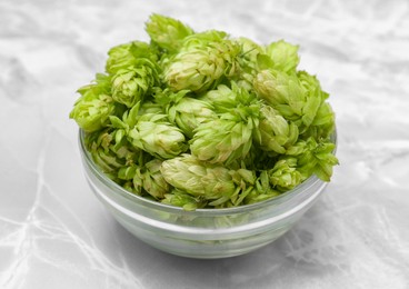 Photo of Bowl of fresh green hops on light grey marble table, closeup