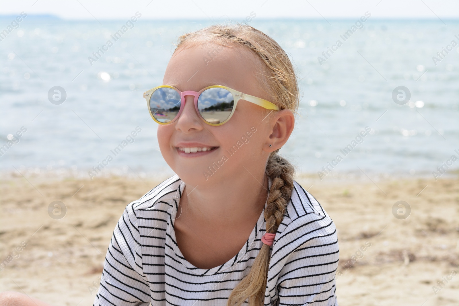 Photo of Little girl wearing sunglasses at beach on sunny day