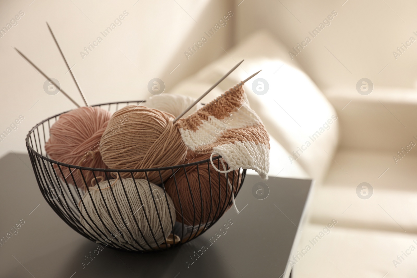 Photo of Yarn balls and knitting needles in metal basket on grey table indoors, space for text. Creative hobby