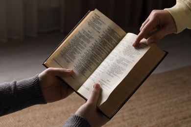 Photo of Woman showing psalm in Bible to man indoors, closeup