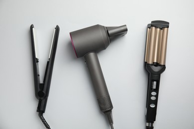 Hair dryer, straightener and triple curling iron on light grey background, flat lay