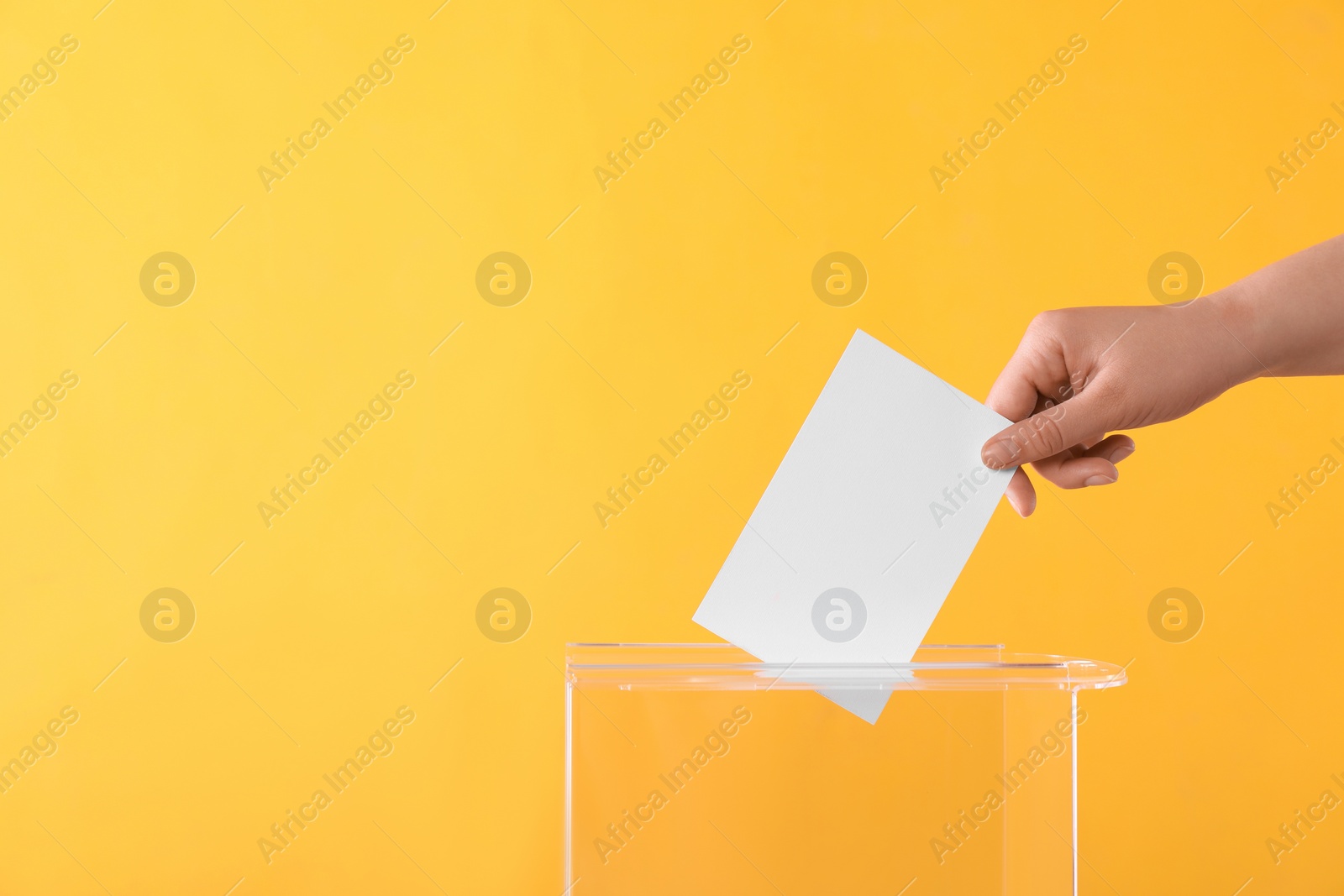 Photo of Woman putting her vote into ballot box on orange background, closeup. Space for text