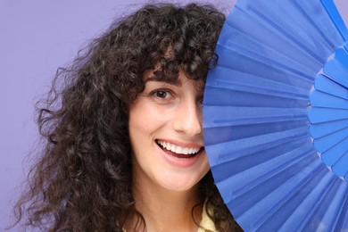 Photo of Happy woman holding hand fan near her face on purple background