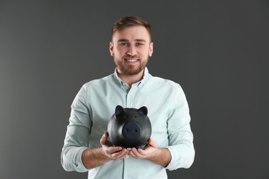 Photo of Portrait of happy young man with piggy bank on grey background. Money saving
