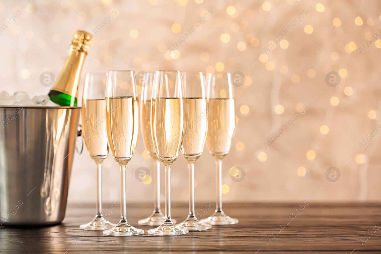 Photo of Glasses with champagne and bottle in bucket on table against blurred lights