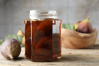 Photo of Jar of tasty sweet jam and fresh figs on wooden table. Space for text