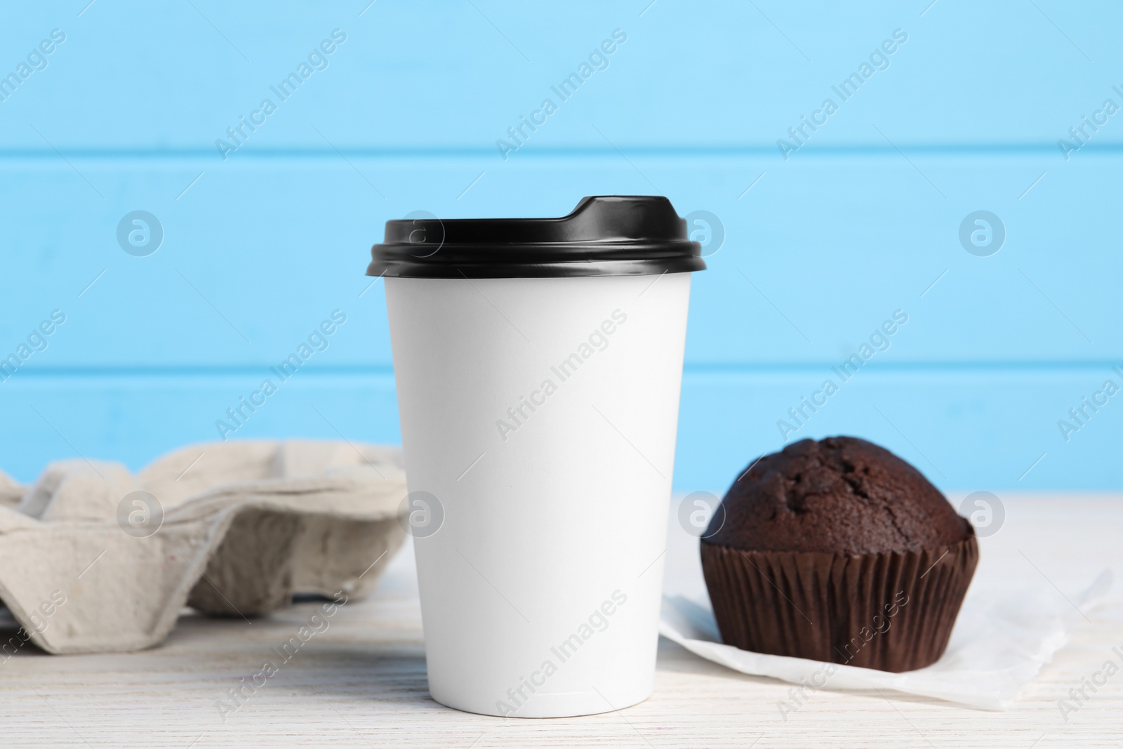 Photo of Paper cup with black lid and muffin on white wooden table. Coffee to go