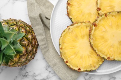 Slices of tasty ripe pineapple and whole fruit on white marble table, flat lay