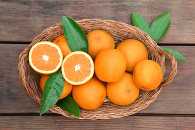 Wicker basket with ripe juicy oranges and green leaves on wooden table, top view