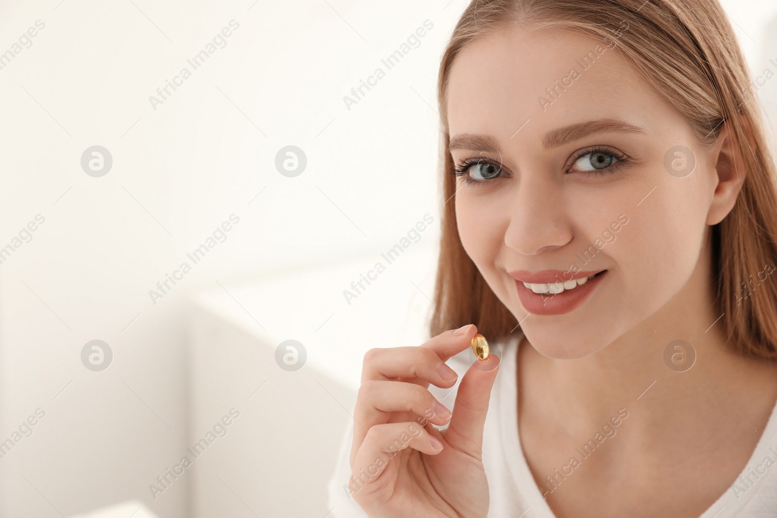 Photo of Young woman taking vitamin capsule on light background. Space for text