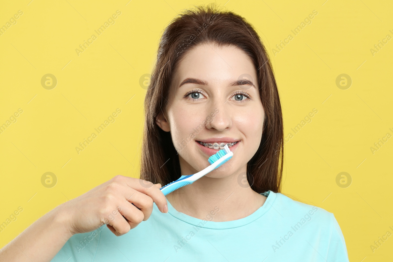 Photo of Smiling woman with dental braces cleaning teeth on yellow background