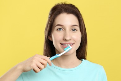 Smiling woman with dental braces cleaning teeth on yellow background