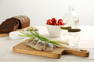 Photo of Wooden board with delicious salted herring slices and green onion on white table