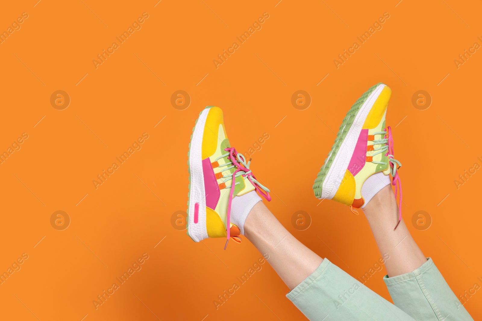 Photo of Woman wearing pair of new stylish sneakers on orange background, closeup. Space for text