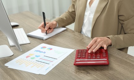 Photo of Professional accountant using calculator at wooden desk in office, closeup