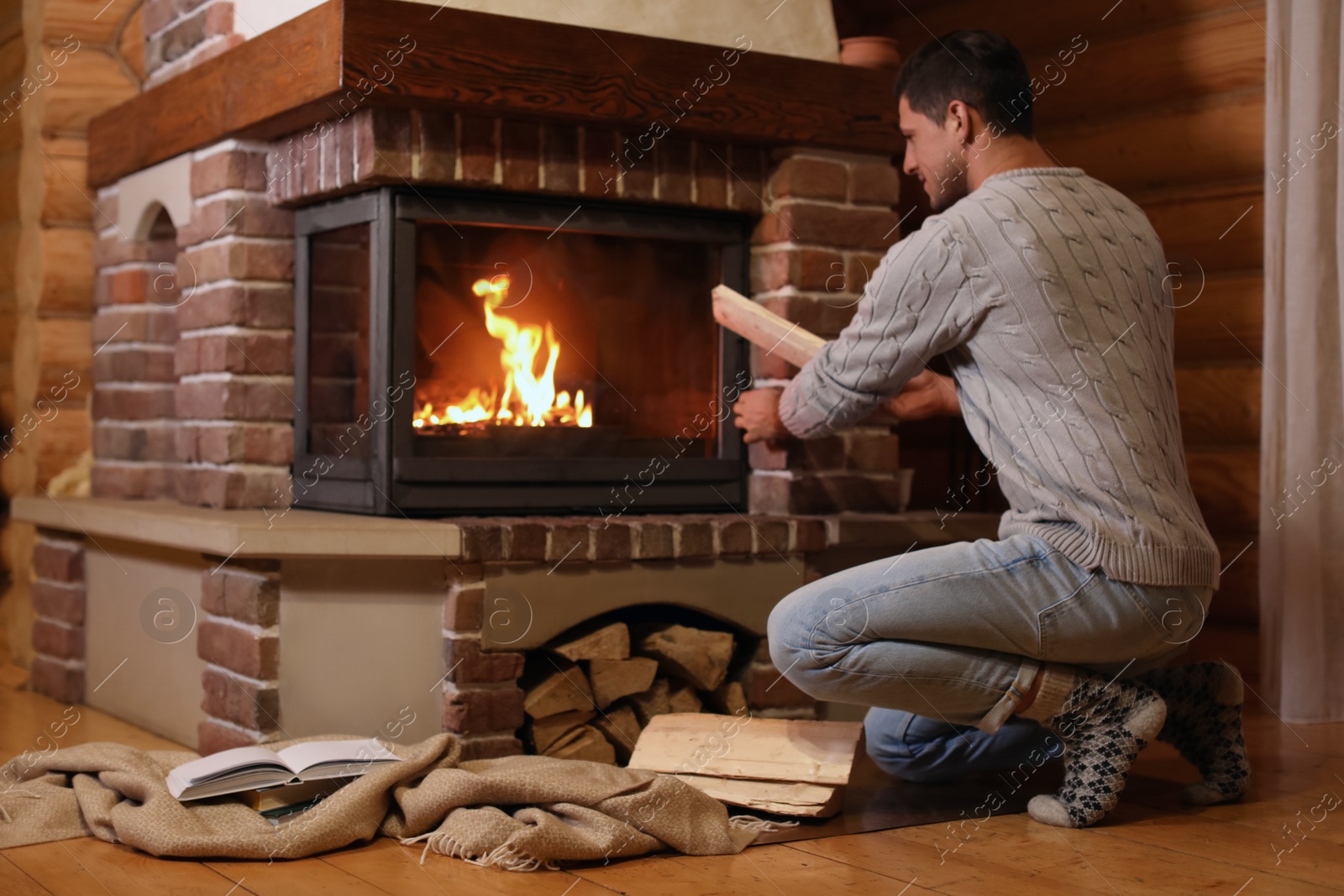 Photo of Man putting dry firewood into fireplace at home. Winter vacation