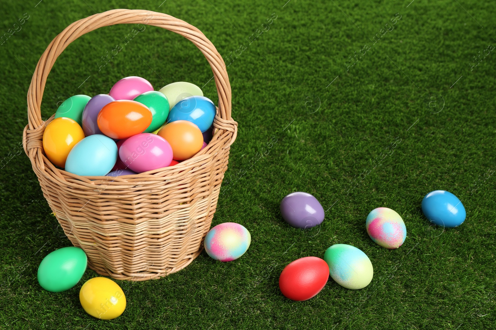 Photo of Wicker basket with bright painted Easter eggs on green grass