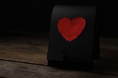 Torn black sheet with heart sticker on wooden table, space for text. Relationship problems concept