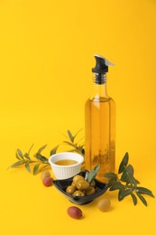 Photo of Oil, olives and tree twigs on yellow background