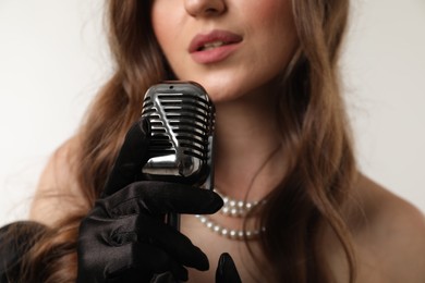 Photo of Woman with microphone singing on light background, selective focus