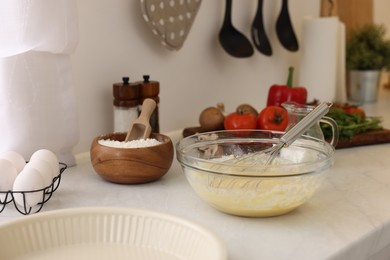 Metal whisk, cream in bowl and different products on light table indoors