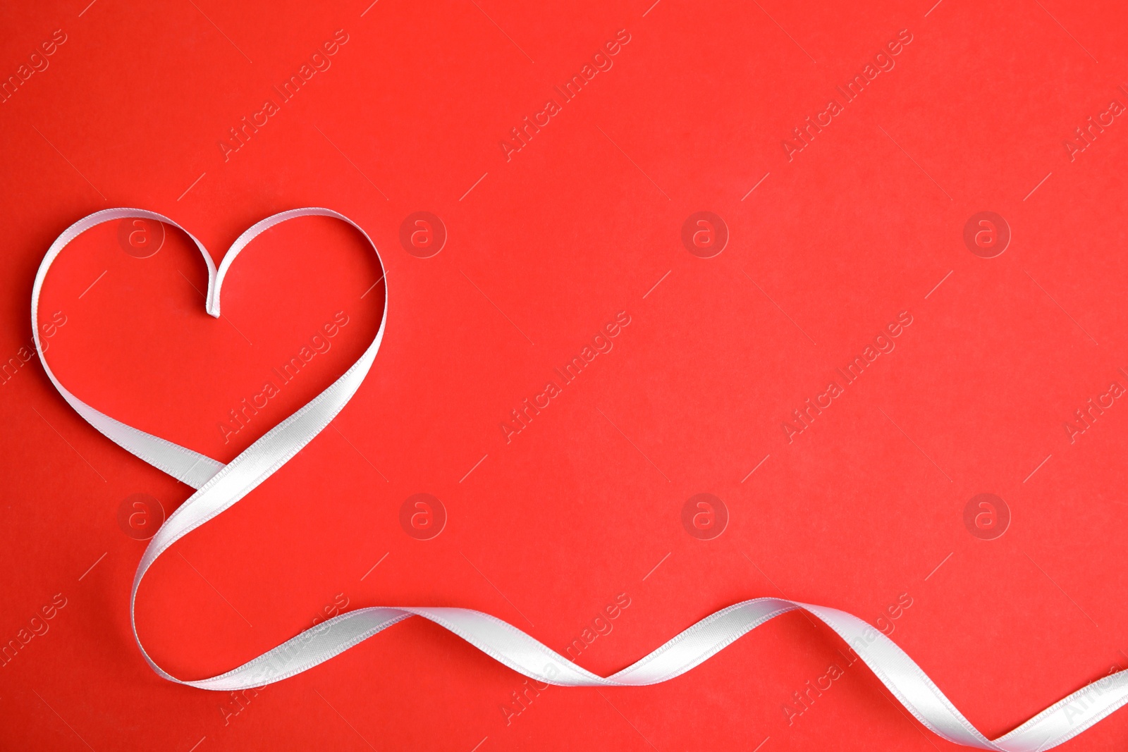 Photo of Heart made of white ribbon on red background, top view with space for text. Valentine's day celebration