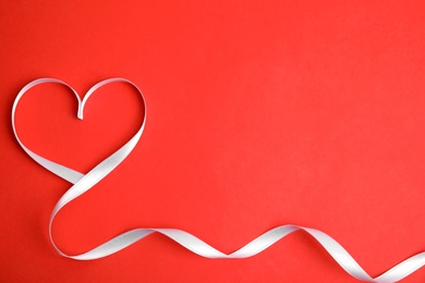 Photo of Heart made of white ribbon on red background, top view with space for text. Valentine's day celebration