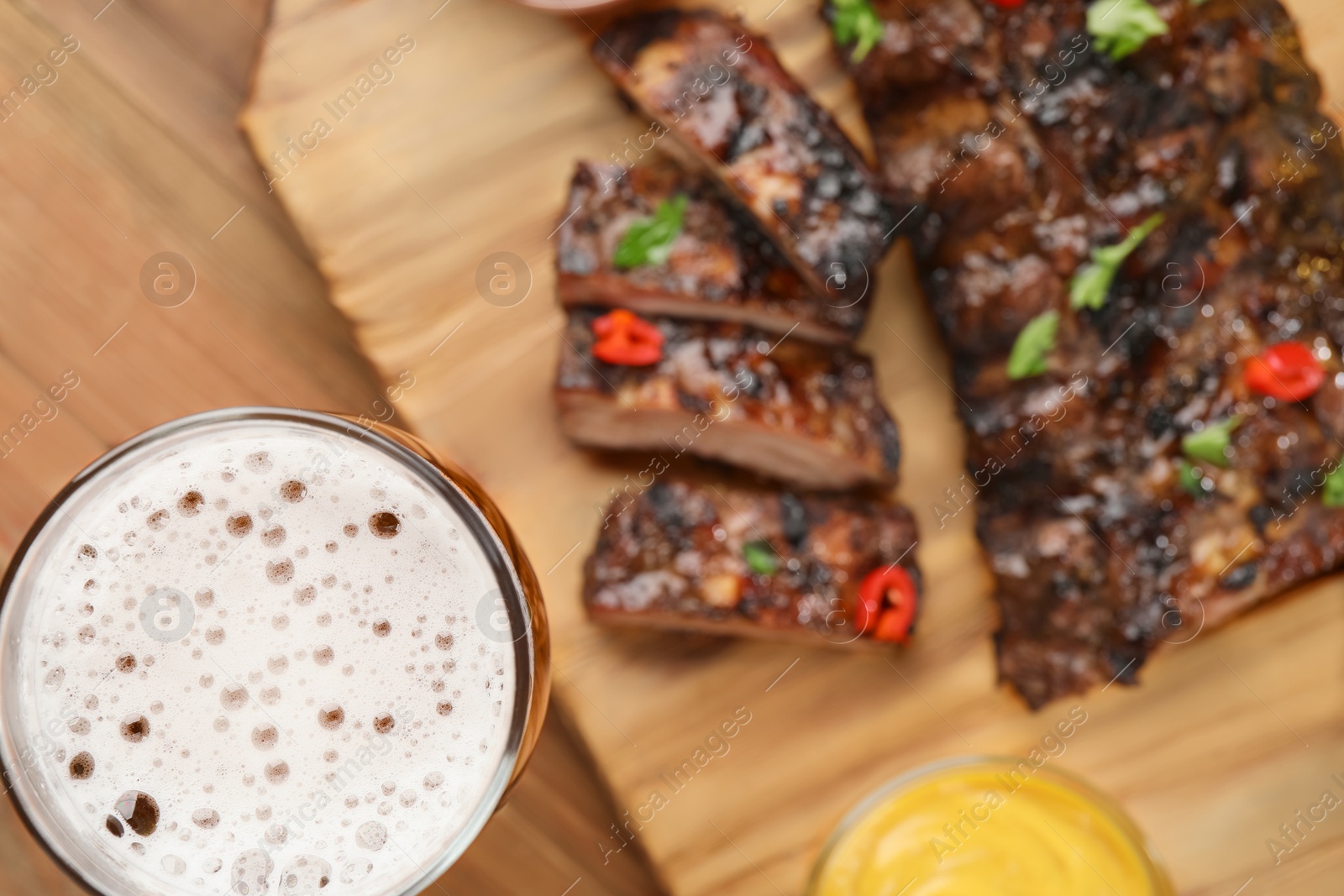 Photo of Glass of beer, tasty grilled ribs and sauces on wooden table, flat lay