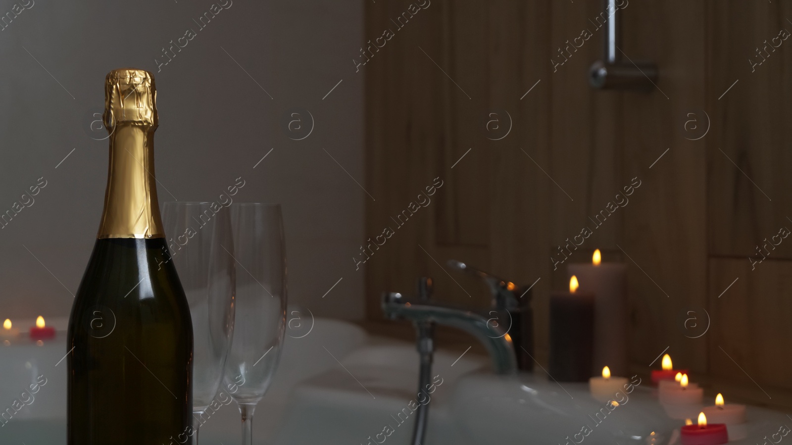 Photo of Bottle of champagne, glasses and burning candles near jacuzzi in bathroom, closeup