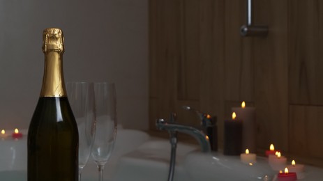 Bottle of champagne, glasses and burning candles near jacuzzi in bathroom, closeup