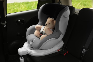 Photo of Teddy bear in child safety seat inside car. Danger prevention