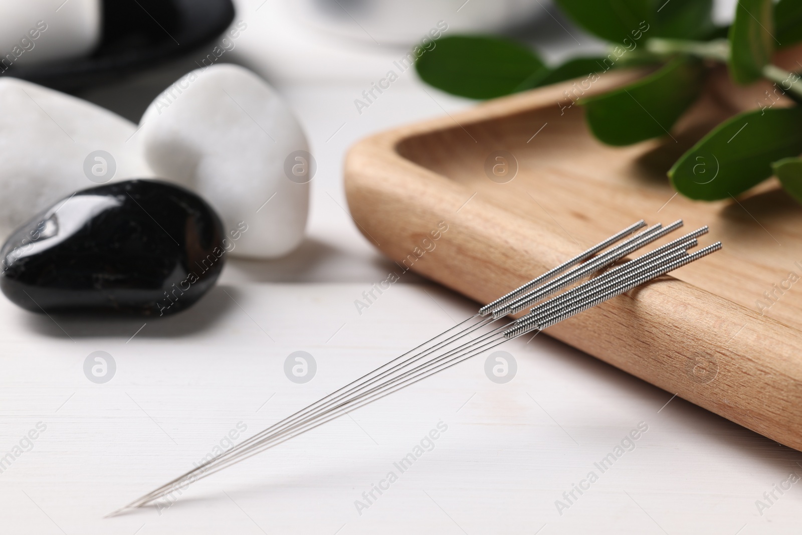 Photo of Board with acupuncture needles on white wooden table