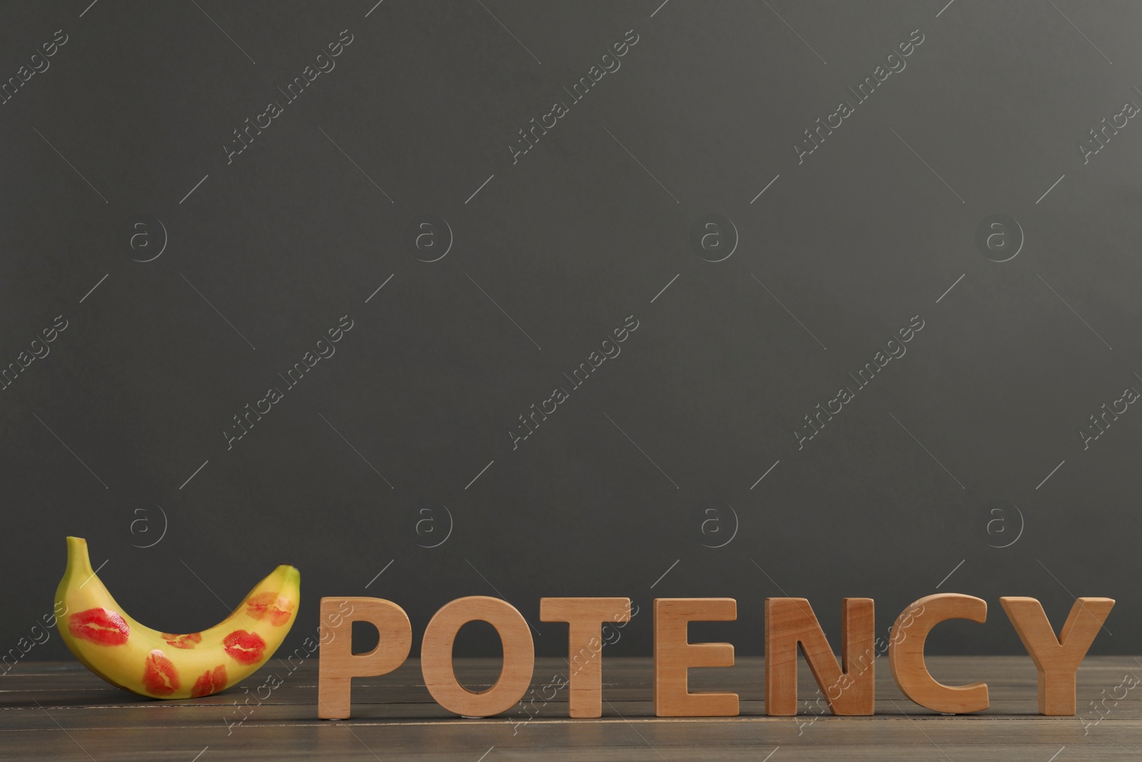 Photo of Word Potency made of letters and banana with red lipstick marks on wooden table against grey background, space for text