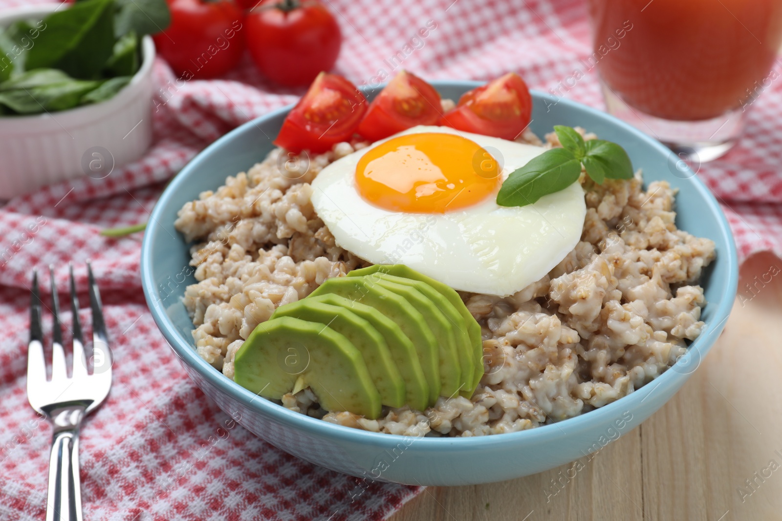 Photo of Delicious boiled oatmeal with fried egg, bacon, avocado and tomato served on wooden table, closeup