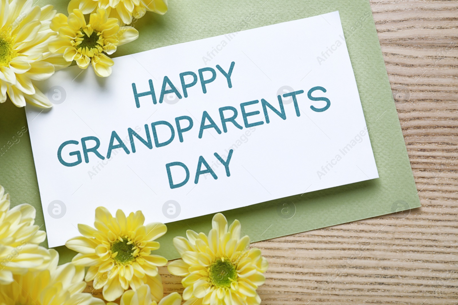 Photo of Beautiful yellow flowers and card with phrase Happy Grandparents Day on wooden background, flat lay