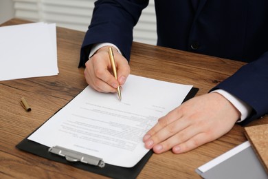 Photo of Man signing document at wooden table, closeup