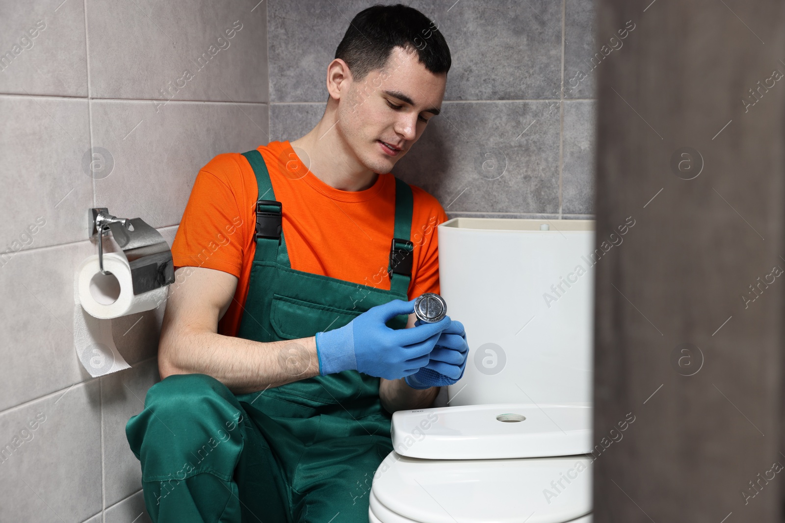 Photo of Young plumber repairing toilet bowl in water closet