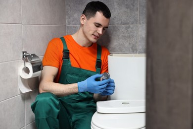 Young plumber repairing toilet bowl in water closet