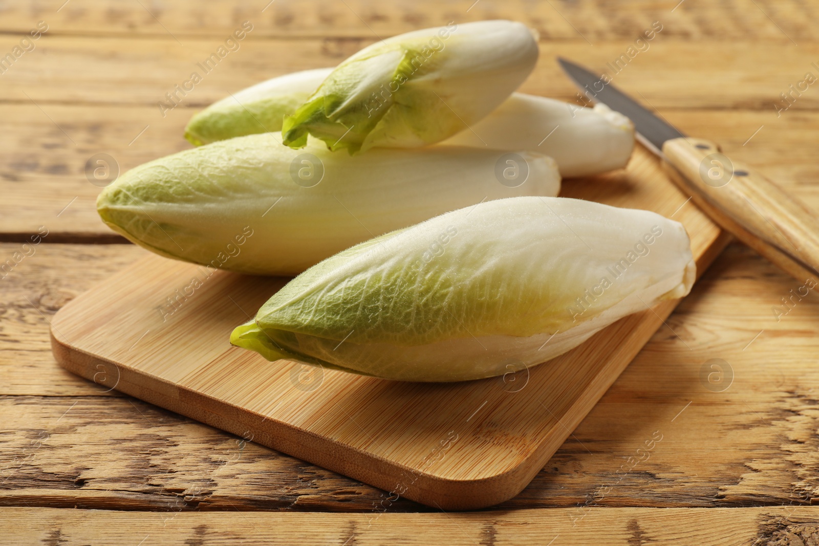 Photo of Fresh raw Belgian endives (chicory), board and knife on wooden table, closeup