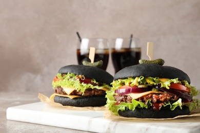 Photo of Board with black burgers on table against color background. Space for text