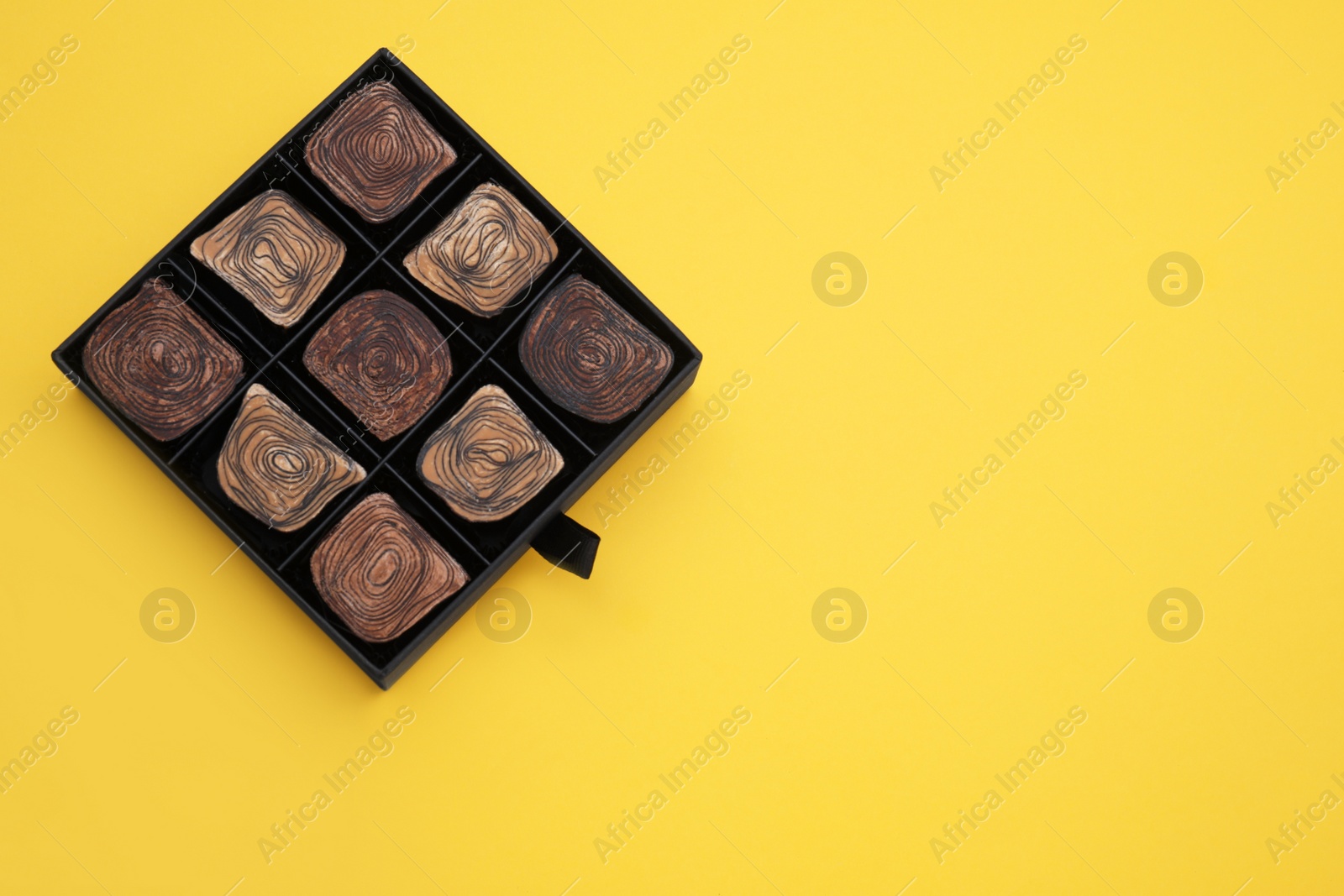 Photo of Box of tasty chocolate candies on yellow background, top view. Space for text