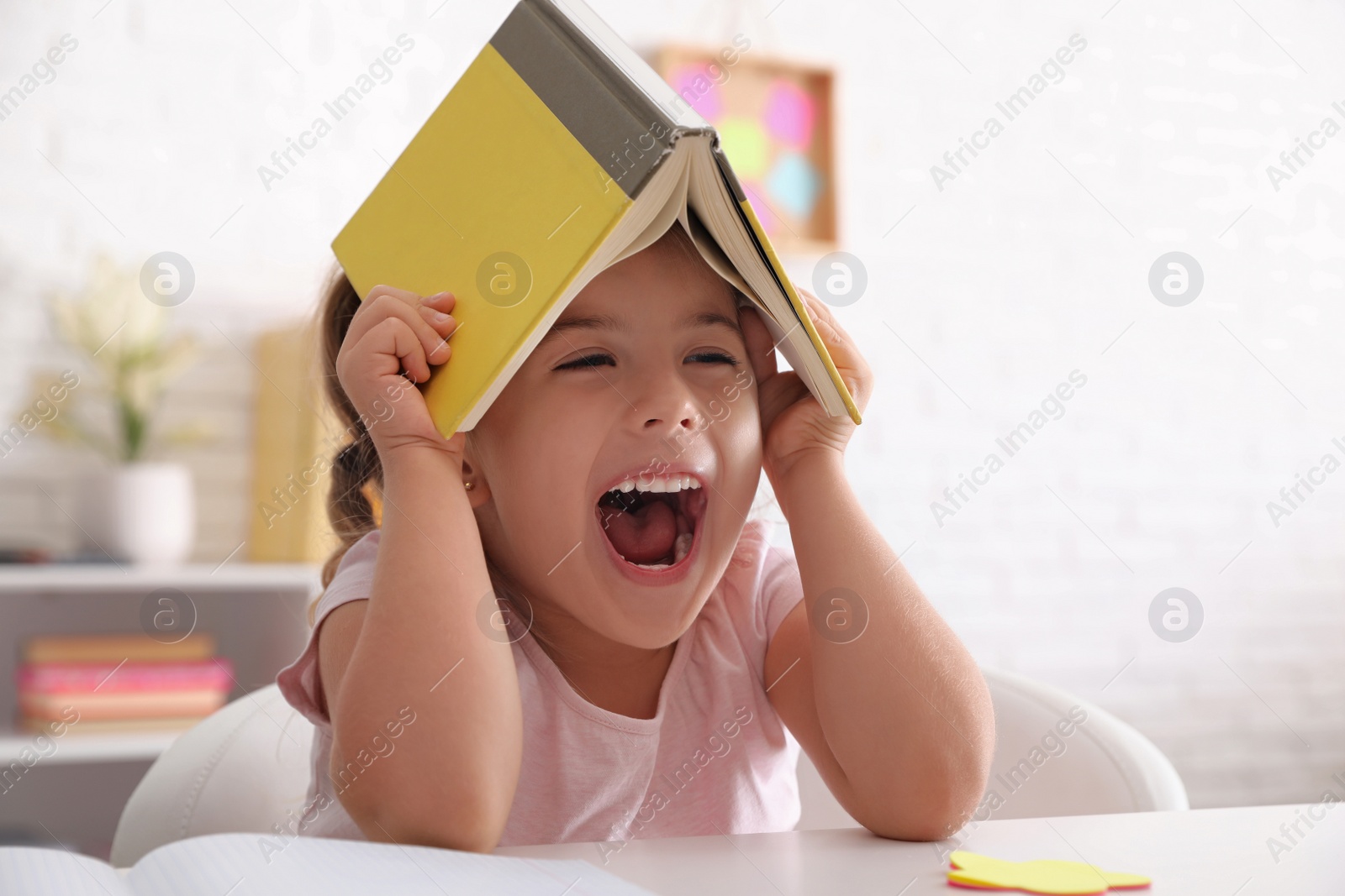 Photo of Emotional little girl playing with book at table. Doing homework
