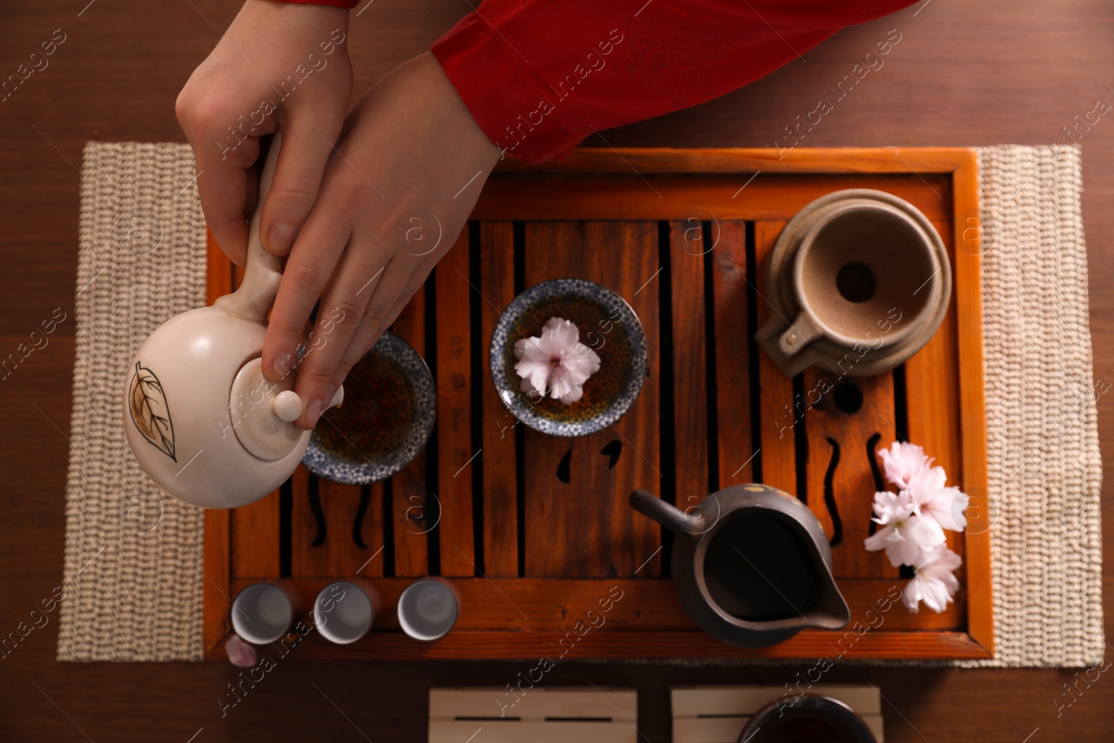 Photo of Master pouring freshly brewed tea into cup during traditional ceremony at table, top view