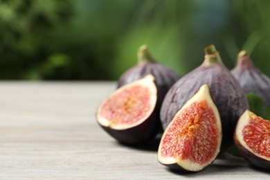 Photo of Whole and cut ripe figs on light wooden table against blurred green background, closeup. Space for text