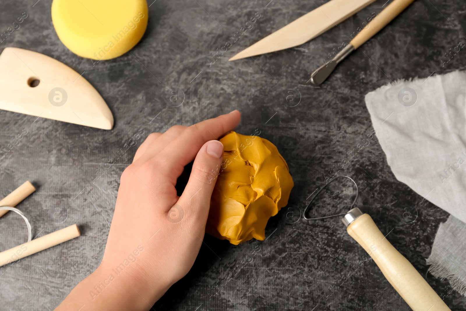 Photo of Woman holding clay at grey stone table with modeling tools, closeup